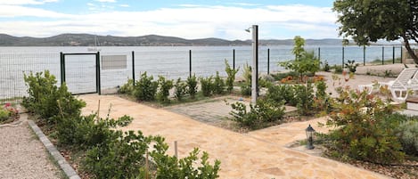 A paved patio with a view of the sea, surrounded by greenery and a fence.