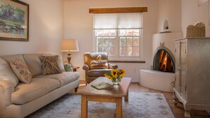 Una sala de estar acogedora con un sofá, una mesa con un jarrón de girasoles, una chimenea y una ventana con persianas.