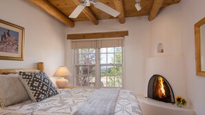 Un dormitorio con una cama grande, chimenea, ventana con vistas y ventilador de techo.