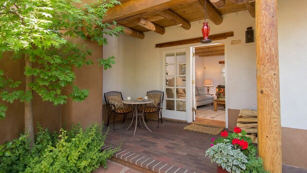Un patio con una pérgola de madera, una mesa con sillas y una puerta que da a una habitación interior.