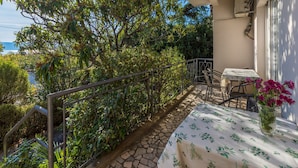 Un balcon agrémenté d’une table et de chaises, entouré d’une végétation luxuriante et offrant une vue sur la mer.