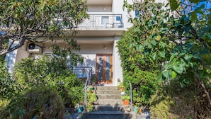 Un bâtiment à deux étages doté d’un balcon, entouré d’une végétation luxuriante et agrémenté de plantes en pot.