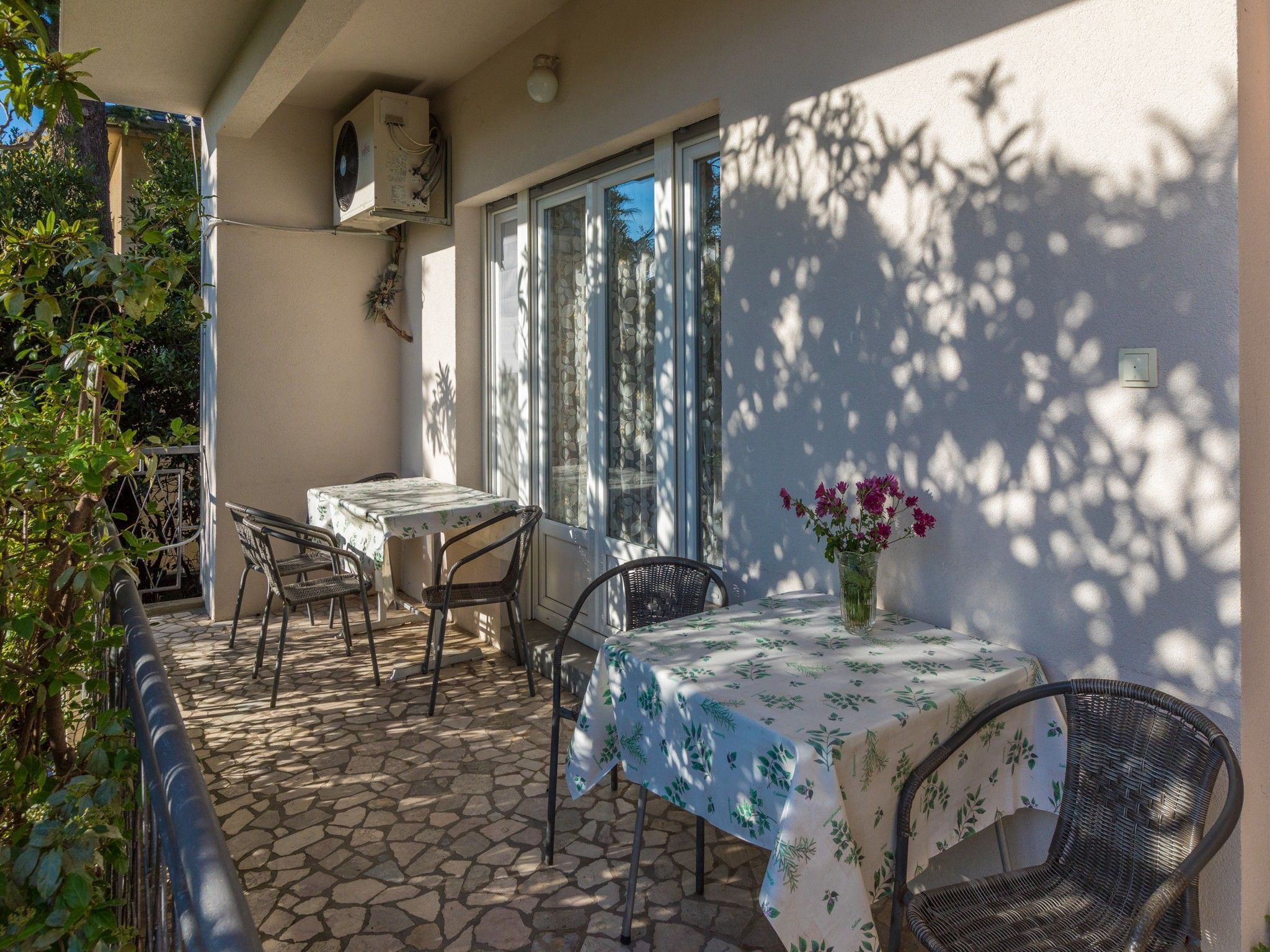 A patio with a table and chairs, a vase with flowers, and a window with curtains.