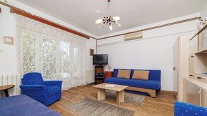 Un salon avec un canapé bleu, deux fauteuils bleus, une table basse en bois et un téléviseur posé sur un meuble.