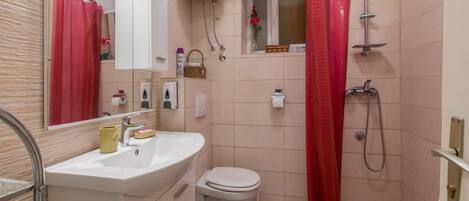 Un baño con un lavamanos blanco, un inodoro, una ducha con cortina roja y un calentador blanco en la pared.