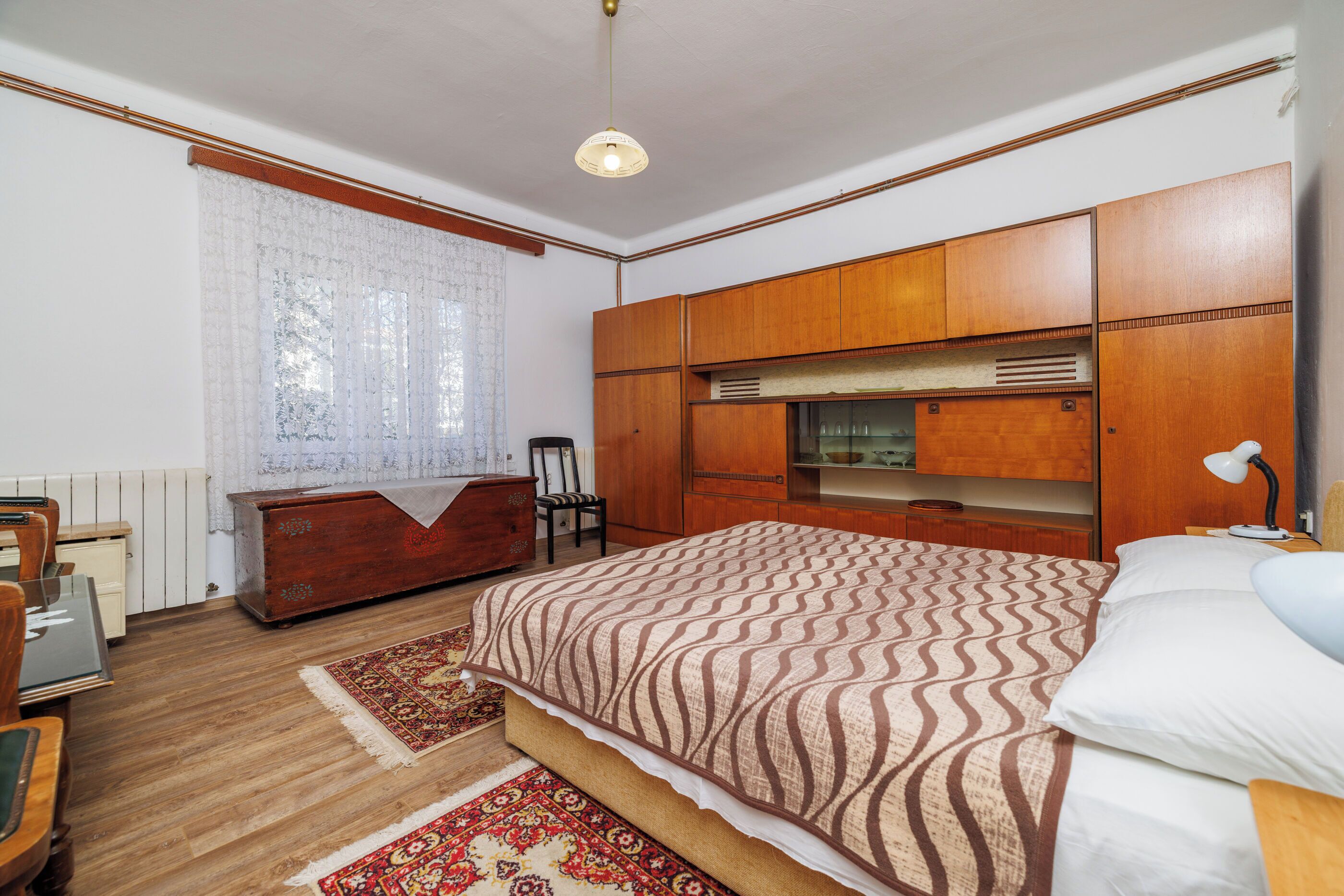 A bedroom with a large bed, wooden wardrobe, a desk, and a chair.