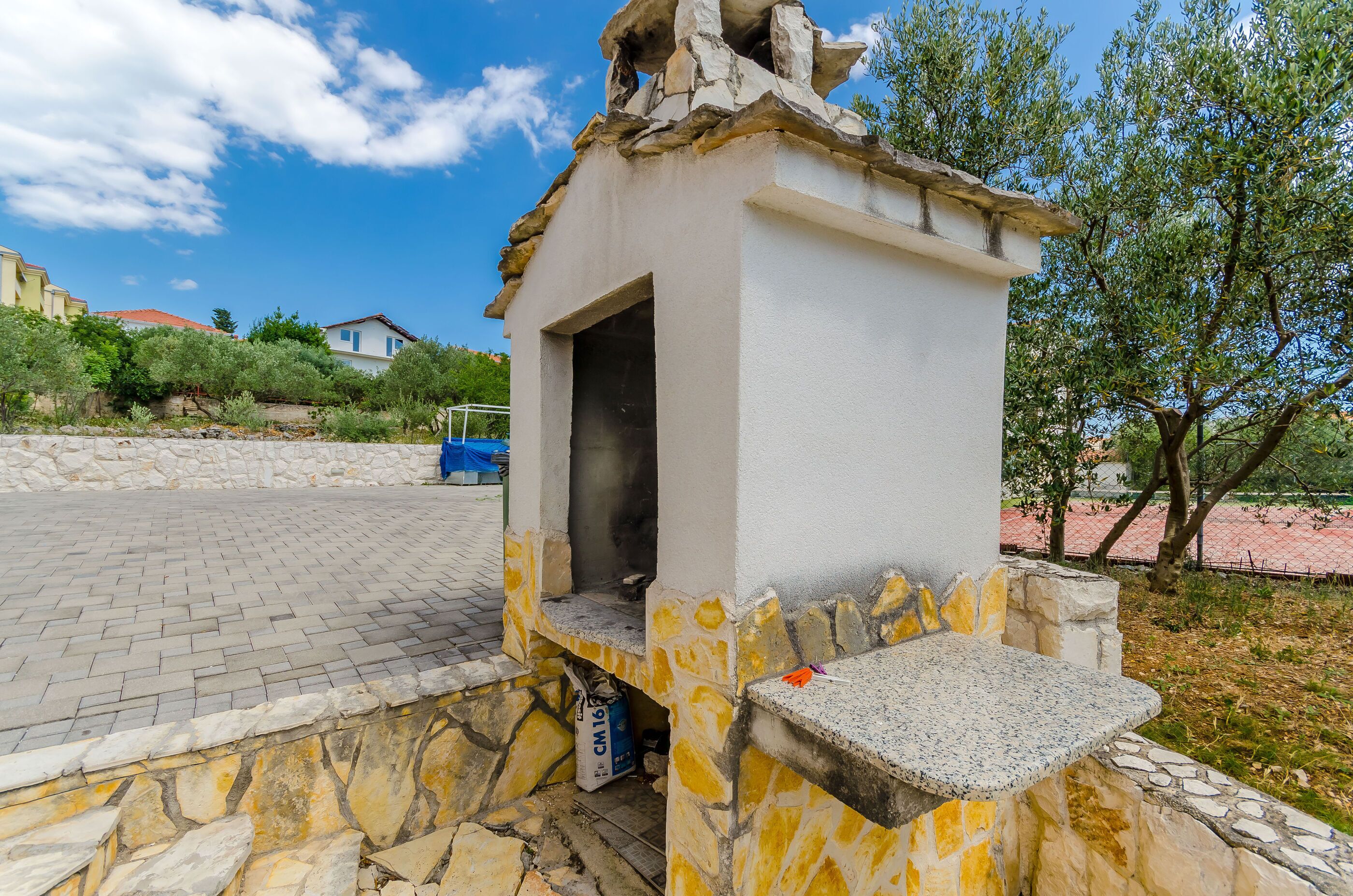 A stone structure with a small opening, possibly a restroom, next to a paved area with a stone wall.
