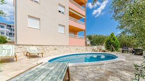 A swimming pool with lounge chairs and a stone wall. - Apartments Melita (Okrug Gornji)