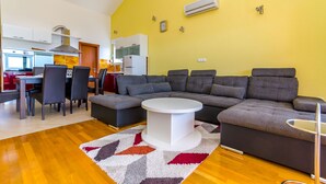 A modern living room with a sectional sofa, a round coffee table, and a dining area with chairs and a table. - Apartments Melita (Okrug Gornji)