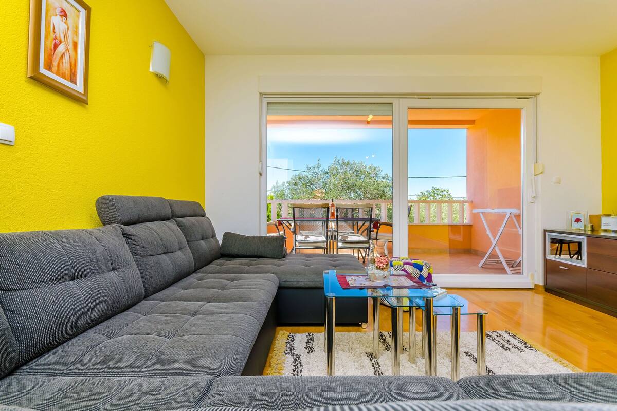 A modern living room with a sectional sofa, a glass coffee table, and a view of a balcony with outdoor furniture.