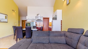 A modern living room with a grey sectional sofa, a dining area with a table and chairs, and a kitchen in the background. - Apartments Melita (Okrug Gornji)