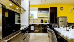 A modern kitchen with a built-in oven, a dining area with a table set for a meal, and a view of the outside through a window. - Apartments Melita (Okrug Gornji)