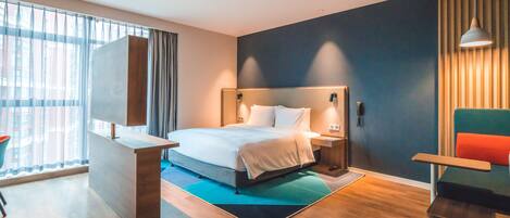 A modern hotel room with a large bed, bedside tables, a desk, and a chair.
