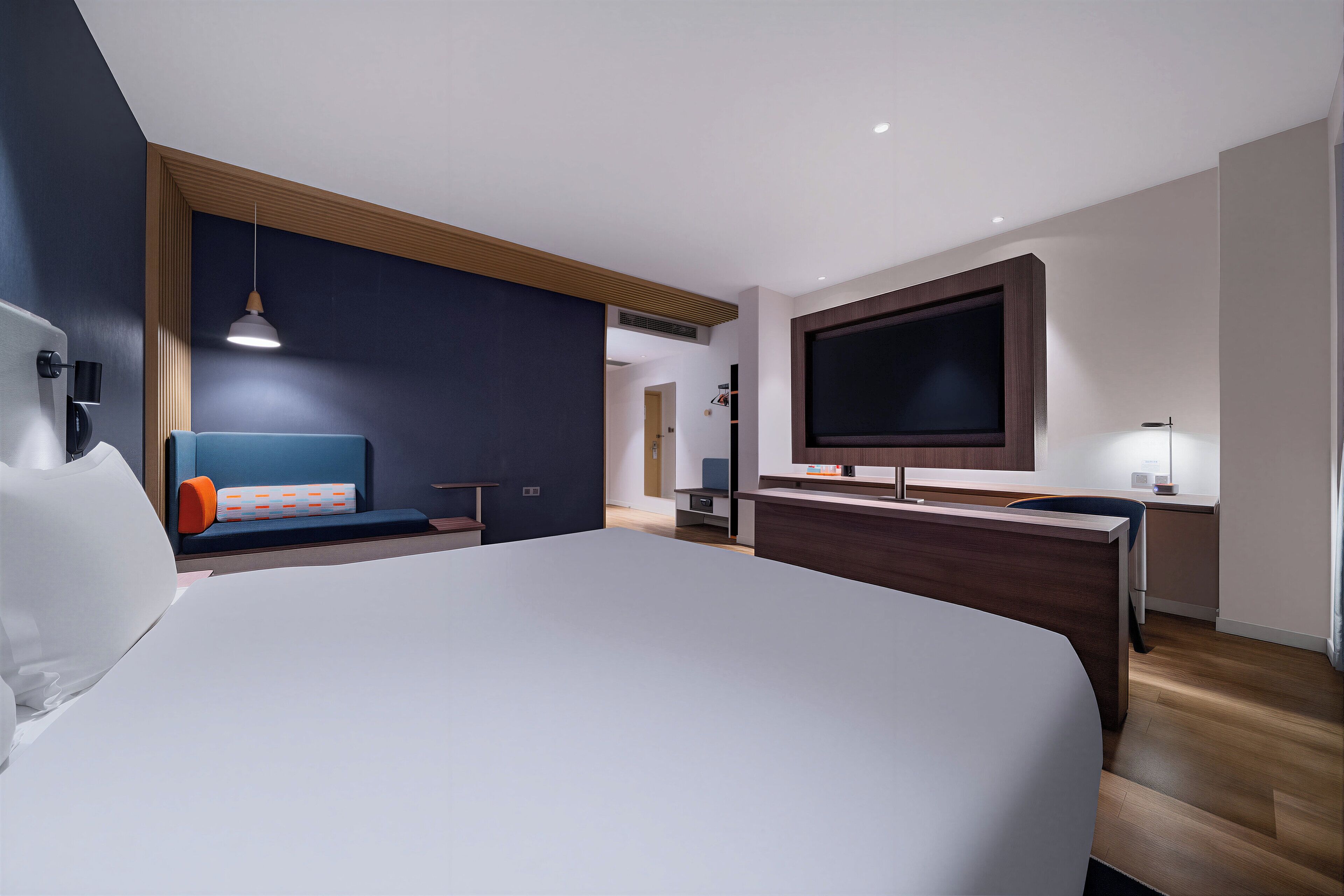 A modern hotel room with a large bed, a desk, a TV, and a seating area.