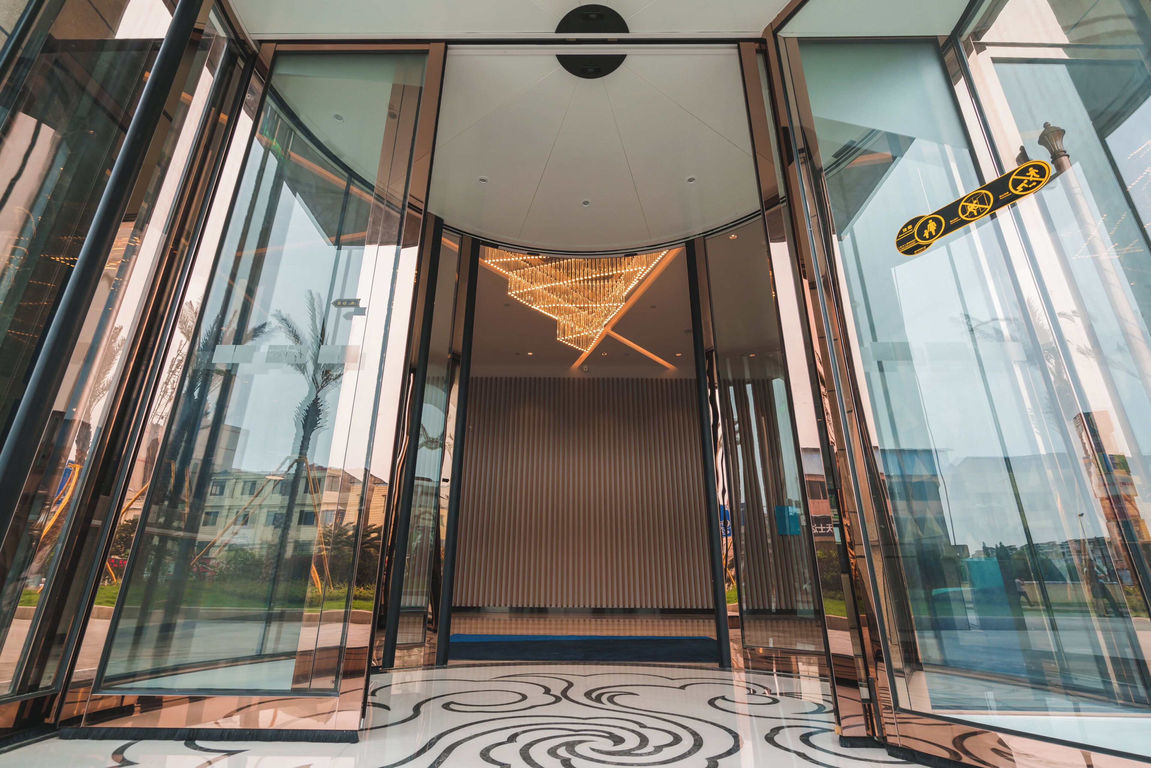 A modern entrance with glass doors, a patterned floor, and a decorative ceiling light fixture.