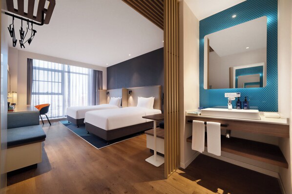Una habitación de hotel moderna con una cama grande, un escritorio, una silla y un baño con espejo y lavamanos.