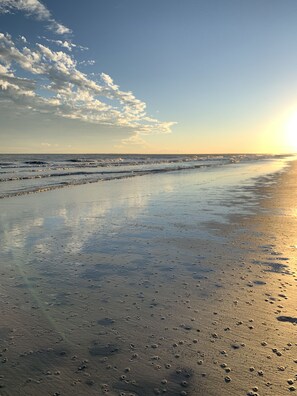 A beach with wet sand and footprints, a clear sky, and the sun setting in the background. - 5 Atlantic Pointe, Beautiful Ocean View Home on Hole #15 of Atlantic Dunes GC (Hilton Head Island)
