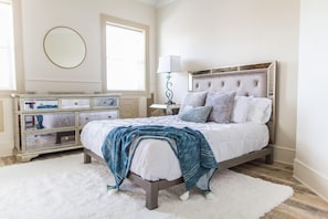 A bedroom with a bed, a dresser, a mirror, and a lamp. - Condos at The Ray (St. Augustine)
