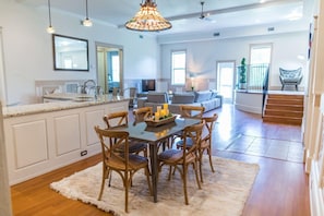 A spacious kitchen with a dining area, wooden chairs, a chandelier, and a view of the living room. - Condos at The Ray (St. Augustine)
