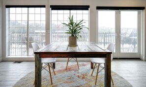 A dining table with a potted plant in the center, surrounded by four white chairs. The room has large windows with a view of outdoor seating. - SCP Depoe Bay (Depoe Bay)