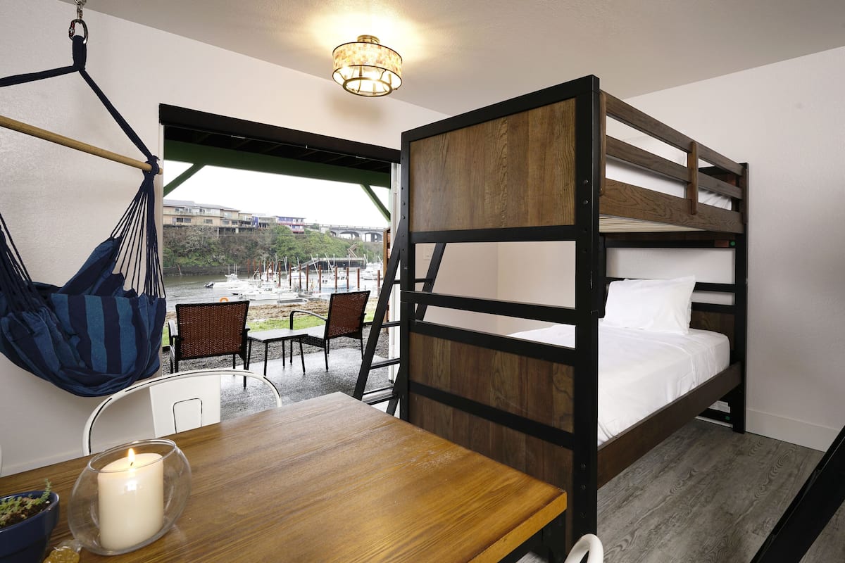 A bunk bed room with a hanging chair, a table with a candle, and a view of a marina.