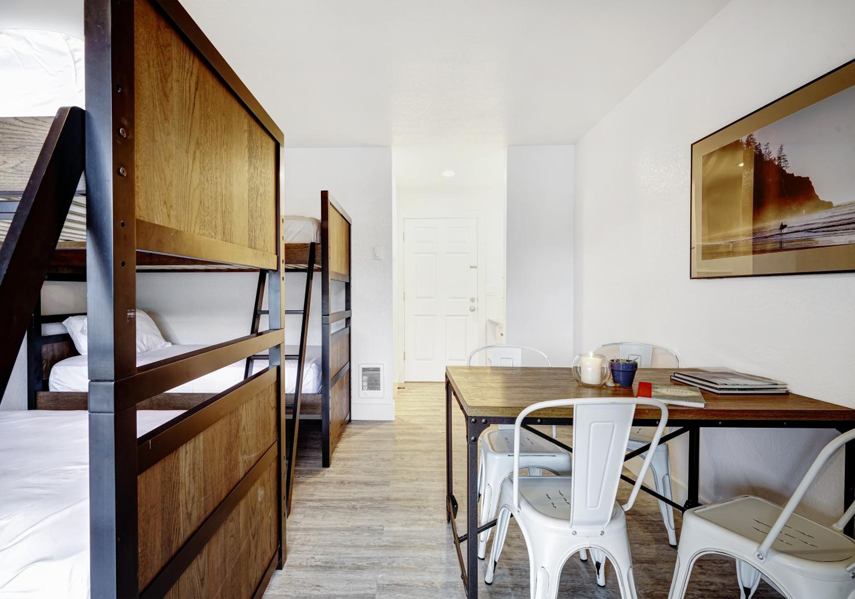 Una habitación con literas, una mesa de comedor con sillas y un cuadro en la pared.