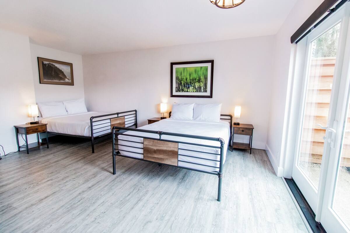 A bedroom with two beds, wooden flooring, and a large window.