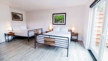 Un dormitorio con dos camas, piso de madera y un ventanal grande.