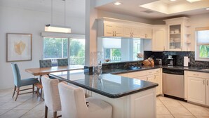 Una cocina moderna con armarios blancos, una isla grande y una zona de comedor con sillas.