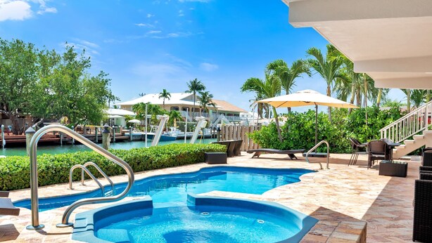 Una piscina con hidromasaje, rodeada de palmeras y mobiliario de exterior.
