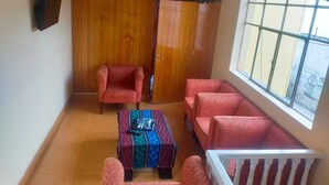 A room with a wooden wardrobe, two patterned armchairs, a small table with a laptop, and a view of the outside through a window. - Hidden Garden - Hostel (Cusco)