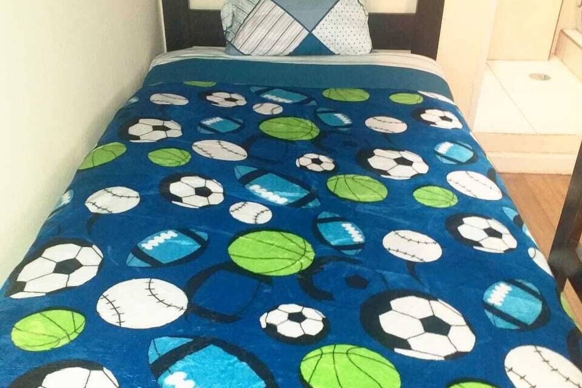 Ein Bett mit einem Bettbezug in blauem Fußballmuster und einem geometrischen Kissen.