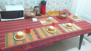 A dining table set with colorful placemats, a red thermos, a microwave, and various kitchen items. - Hidden Garden - Hostel (Cusco)