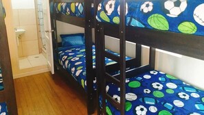 A bunk bed room with a window, a door, and a small bathroom area. - Hidden Garden - Hostel (Cusco)