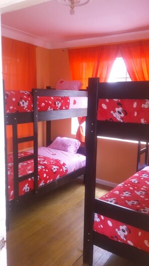 Habitación con literas, colcha de rayas rojas y blancas, cortinas naranjas y piso de madera.