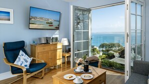 A room with a view of the sea, a wooden desk, a chair, a coffee table with plates and cups, and a television on the wall. - A stunning apartment with breathtaking views, situated in a select development. (Carbis Bay)
