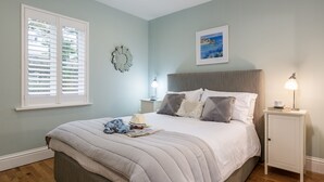 A bedroom with a large bed, a nightstand, a wall clock, and a window with blinds. - A stunning apartment with breathtaking views, situated in a select development. (Carbis Bay)