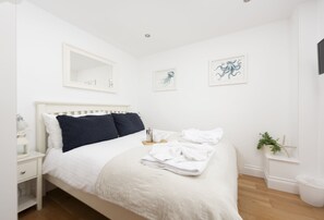 Un lit bien fait, avec une literie blanche et des coussins bleu foncé, une table de chevet avec une lampe et une petite plante en pot posée sur la table de chevet.