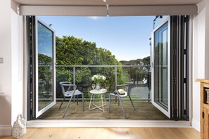 Una habitación con puerta de vidrio corredera que da a un patio exterior. En el interior, hay una pequeña mesa redonda con dos sillas, un jarrón con flores y una cámara sobre la mesa.