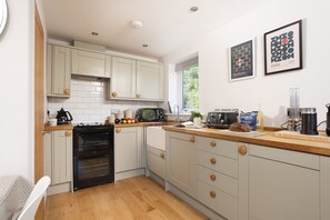 A modern kitchen with light-colored cabinets, a built-in oven, a microwave, and a coffee machine.