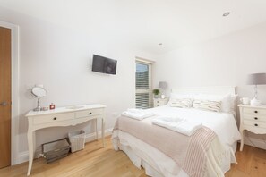 Un dormitorio con cama, mesitas de noche, cómoda, espejo y televisión en la pared.