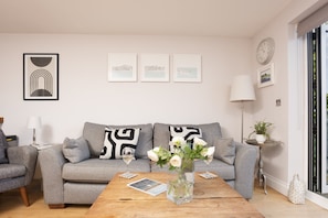 Una sala de estar moderna con un sofá gris, una mesa de centro de madera y un jarrón con flores blancas.