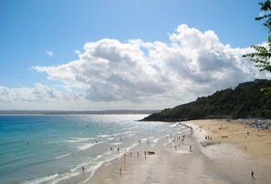 A beach with people walking along the shore, a clear sky, and a distant view of the coastline.