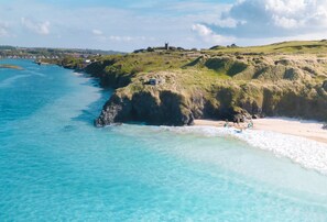 A coastal landscape with clear turquoise waters, grassy hills, and a distant building on a hill.