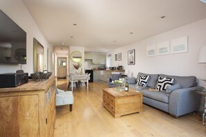 A spacious living room with a grey sofa, wooden coffee table, and a dining area with a table set for two.