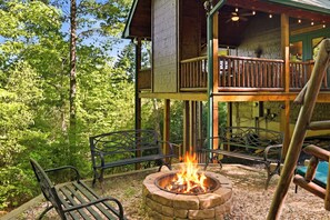 A cabin with a fire pit, outdoor seating, and a deck overlooking a forest.