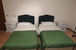 A room with two single beds, each with a green quilt and white pillows, flanked by white nightstands with drawers.