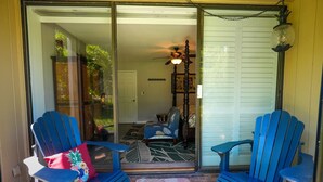 A sliding glass door entrance to a room with two blue Adirondack chairs, a red pillow with a pineapple design, and a small rug.