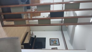 Une pièce avec un sol carrelé, une rambarde en bois, un bureau avec une chaise, un téléviseur et un tableau encadré au mur.