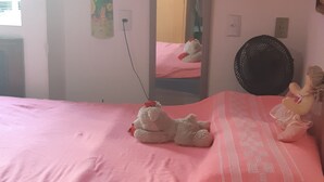 Une chambre avec une couvre-lit rose, un miroir, un ours en peluche et une petite poupée.